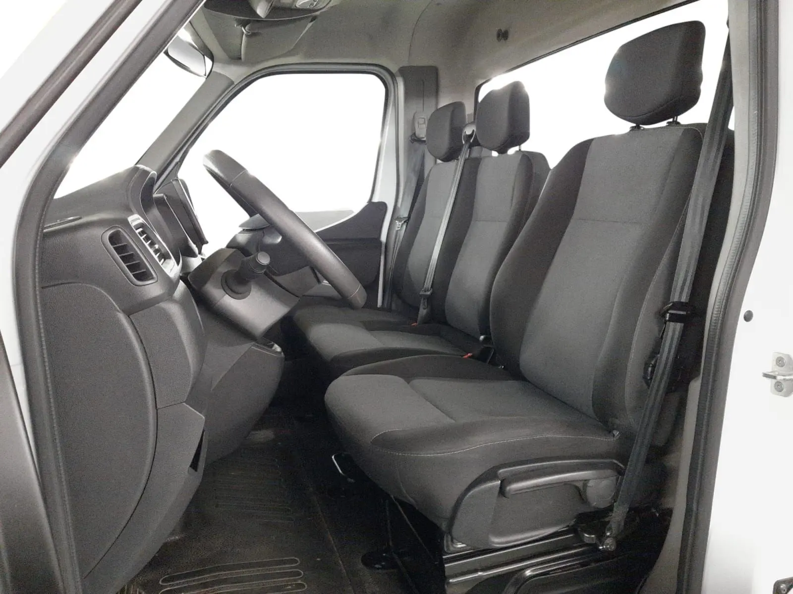 Vue intérieure côté conducteur du Renault Master 2024 blanc, montrant les sièges noirs et le tableau de bord simple.