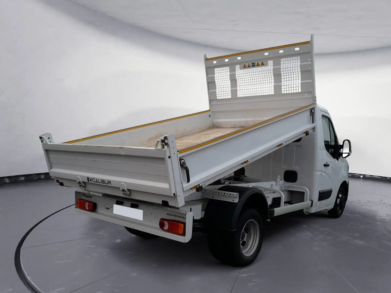 Renault Master blanc vue 3/4 arrière droit avec benne basculante relevée dans un studio.