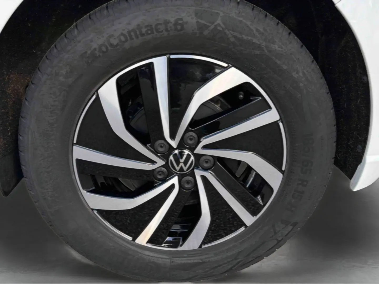 Gros plan sur la jante alliage 15 pouces bicolore noire et argentée d’une Volkswagen Polo blanche, pneu 185/65 R15 visible.