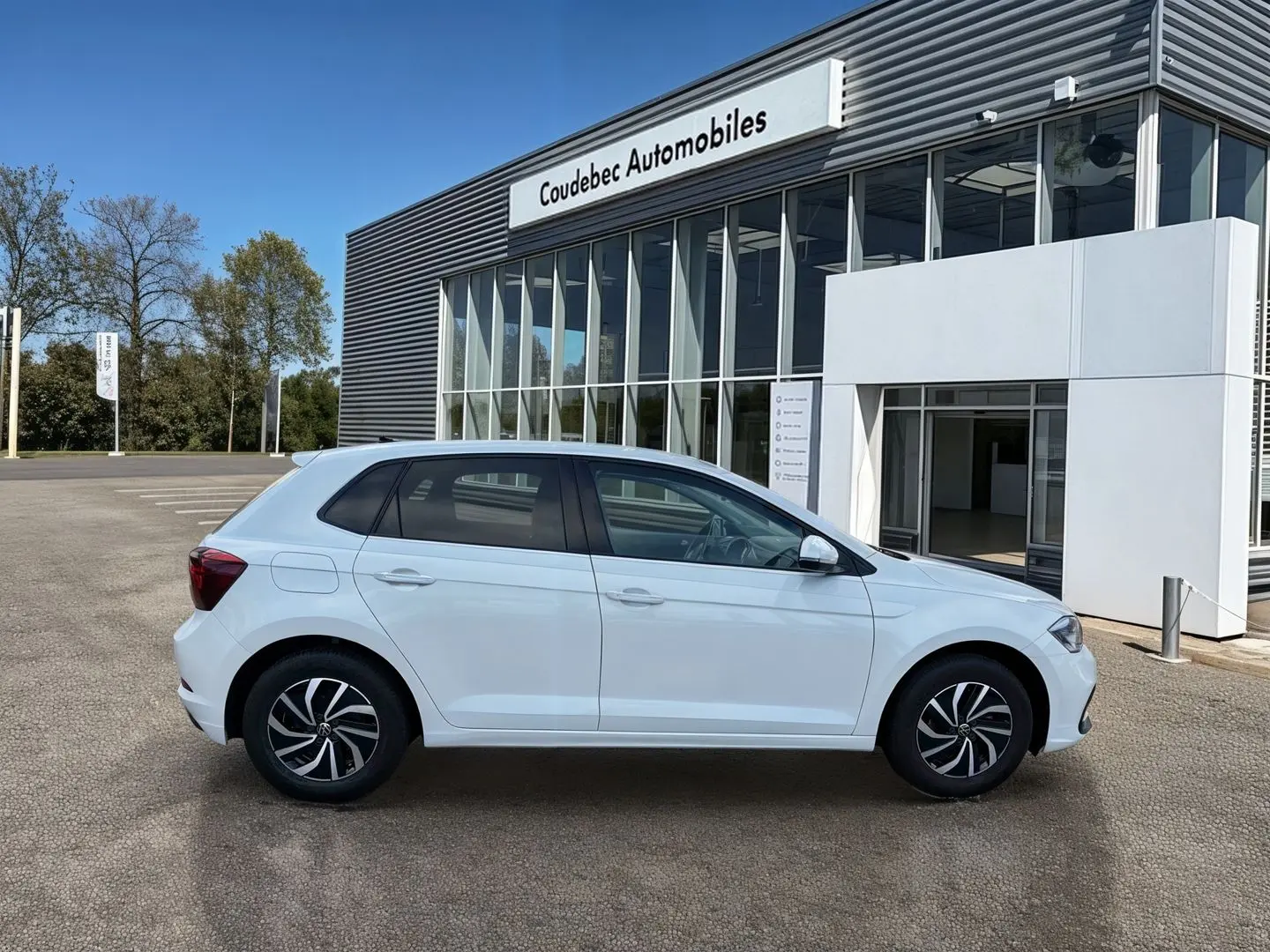 Volkswagen Polo blanche vue de profil côté gauche, garée devant un bâtiment moderne de concession.
