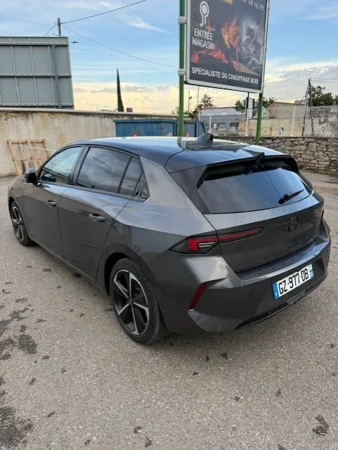 Opel Astra 1.5 Diesel gris vue 3/4 arrière droit, avec feux arrière fins et jantes noires distinctives.