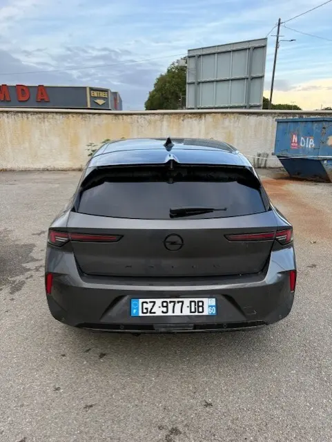 Vue arrière d'une Opel Astra gris foncé 2024 avec vitres teintées et feux arrière étirés, stationnée sur un parking extérieur.