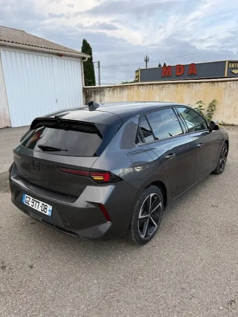 Vue 3/4 arrière droite d'une Opel Astra 2024 gris métallisé avec feux arrière effilés et jantes alliage noires.