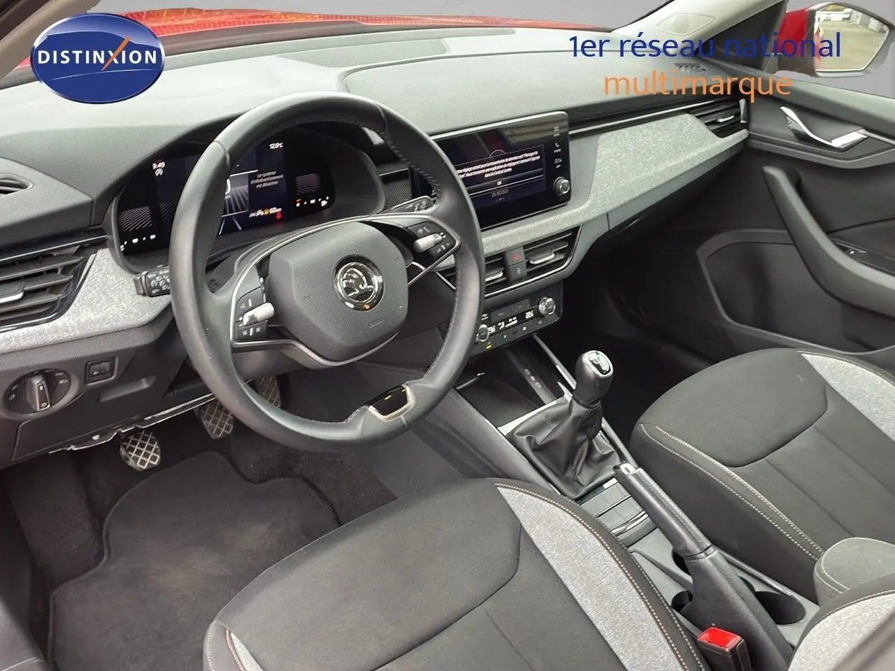 Vue intérieure avant du Skoda Kamiq 2024, montrant le volant, la console centrale avec boîte manuelle et les sièges tissu gris noir.