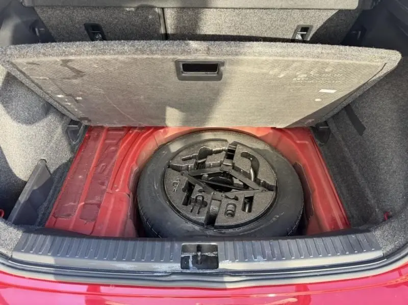 Coffre ouvert d’un SEAT Arona rouge métal 2019, vue plongeante sur la roue de secours et son compartiment.