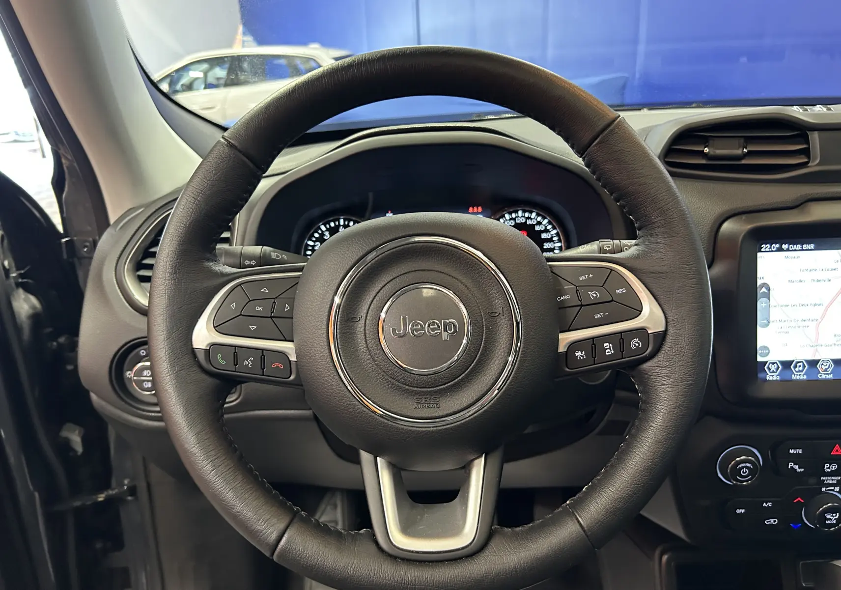 Vue intérieure centrée sur le volant en cuir noir du Jeep Renegade 2023 avec tableau de bord et écran tactile GPS visible.