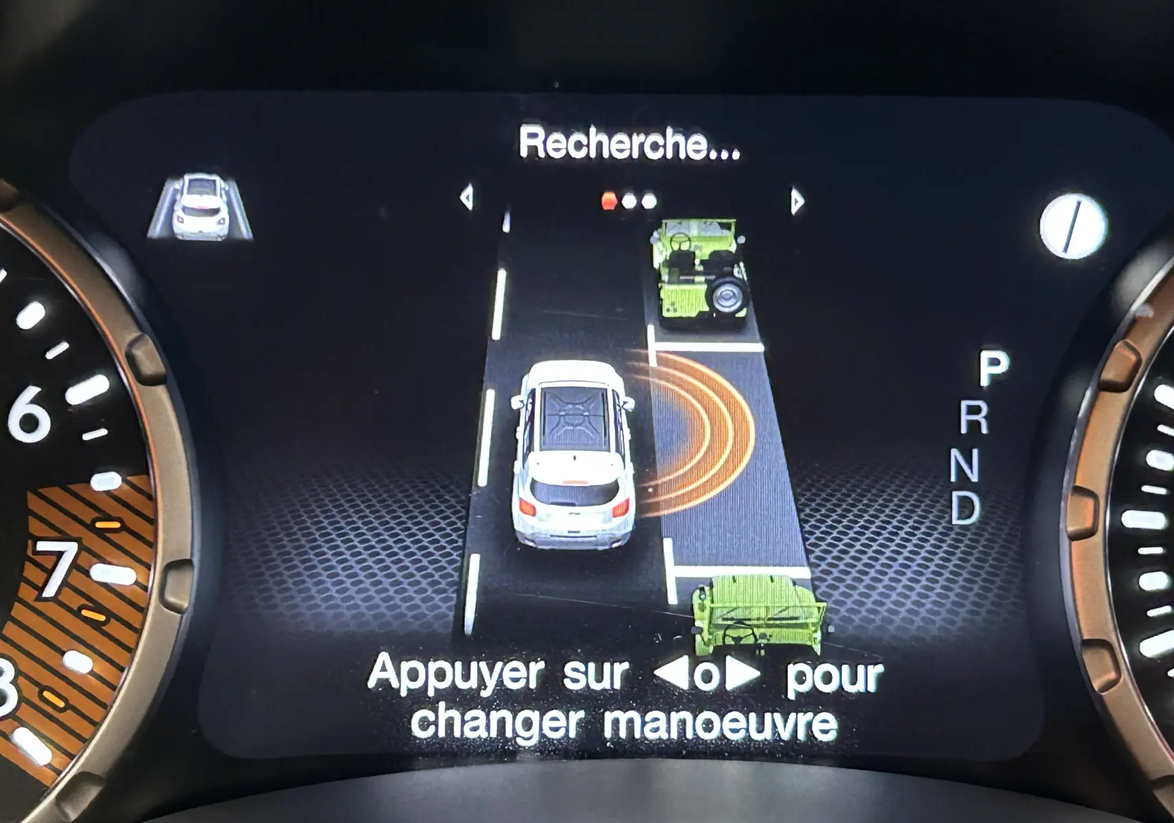 Affichage numérique du tableau de bord montrant l'assistance au stationnement avec vue du véhicule blanc en manœuvre.