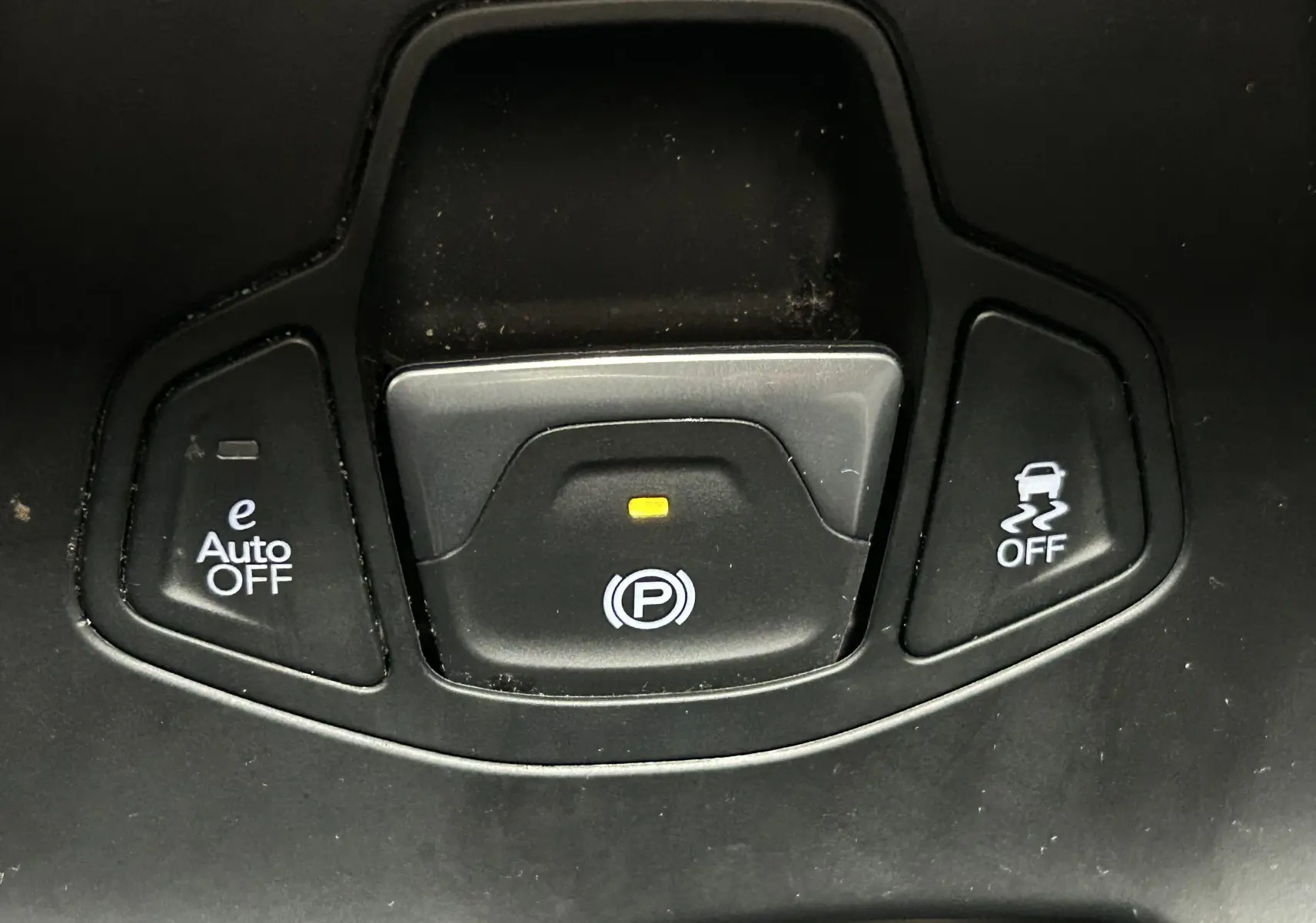 Gros plan sur les boutons de commande du frein à main électronique et des aides à la conduite dans une Jeep Renegade gris graphite.