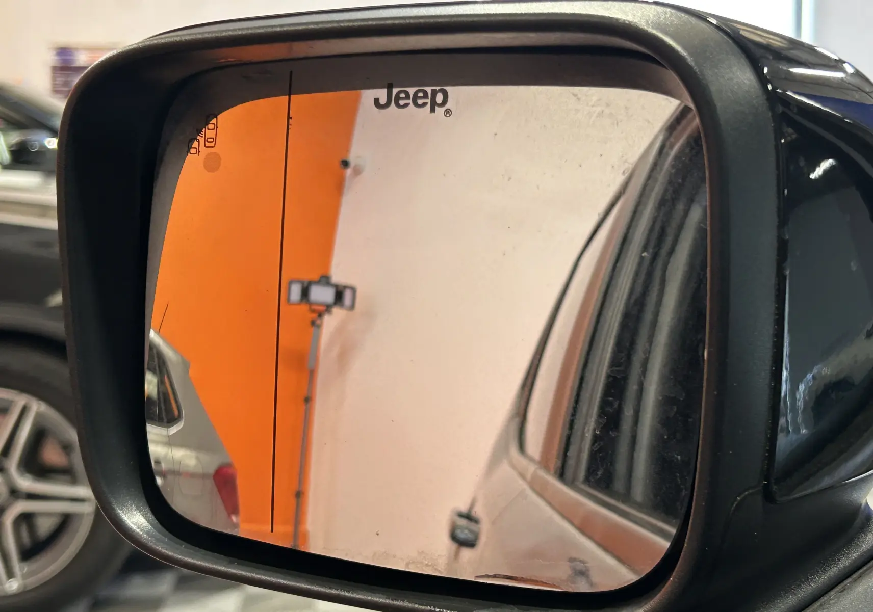 Rétroviseur extérieur gauche d'une Jeep Renegade gris graphite, avec reflet partiel du véhicule et logo Jeep.