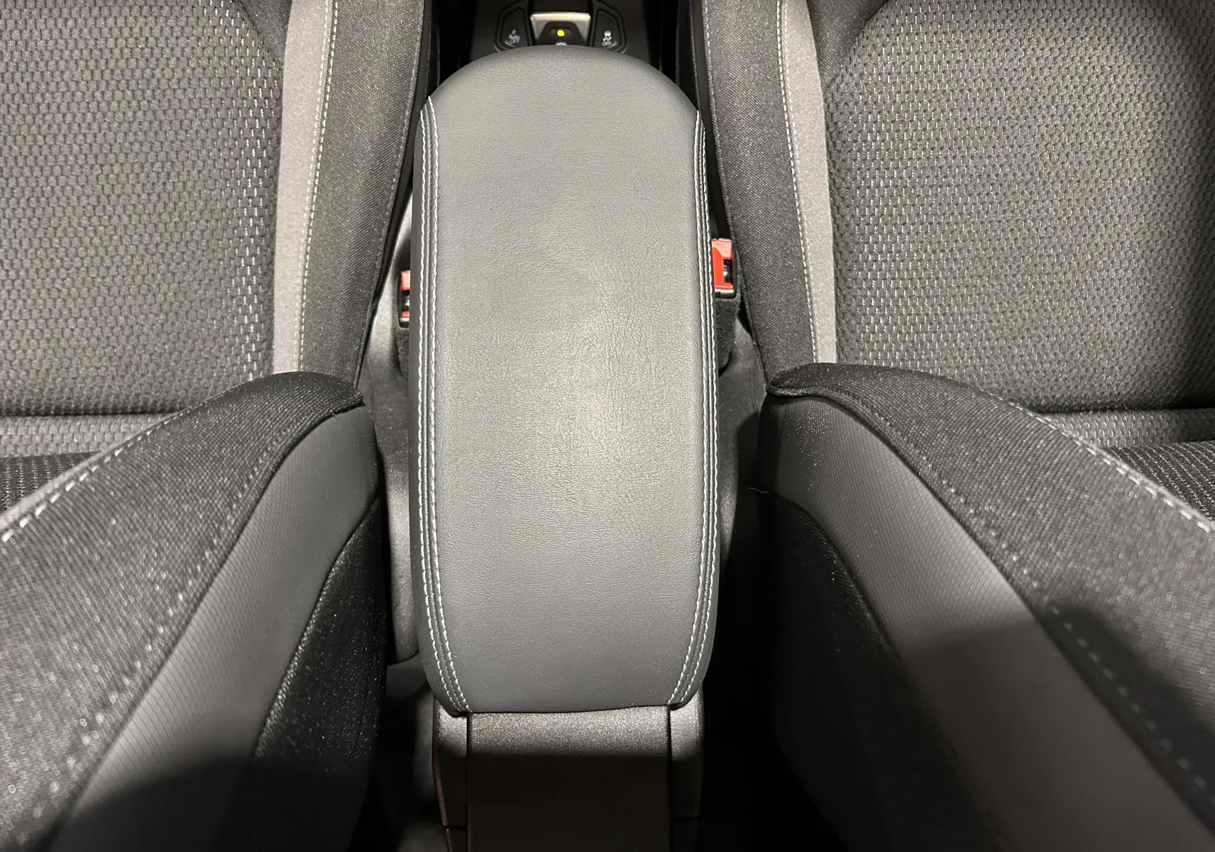 Vue plongeante sur l'accoudoir central en cuir noir avec surpiqûres blanches entre les sièges tissu gris du Jeep Renegade 2023.