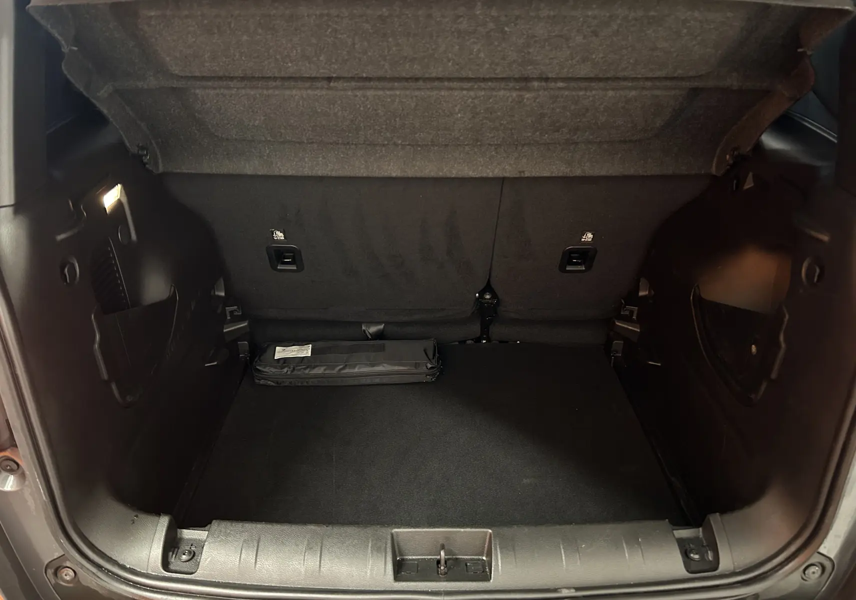 Coffre ouvert de Jeep Renegade gris graphite, vue arrière montrant l’espace de rangement et un kit plié au sol.