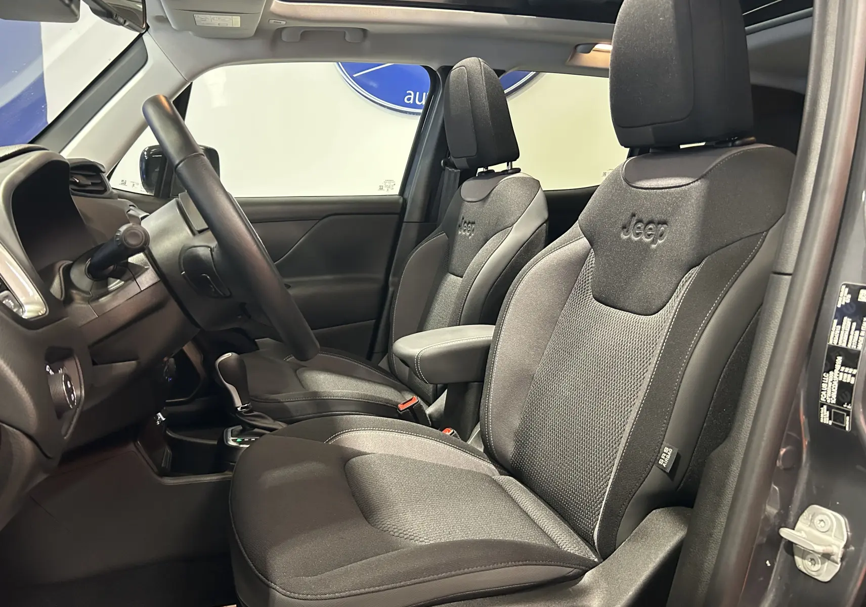 Vue intérieure côté conducteur du Jeep Renegade gris graphite 2023, sièges avant noirs avec logo Jeep et toit ouvrant visible.