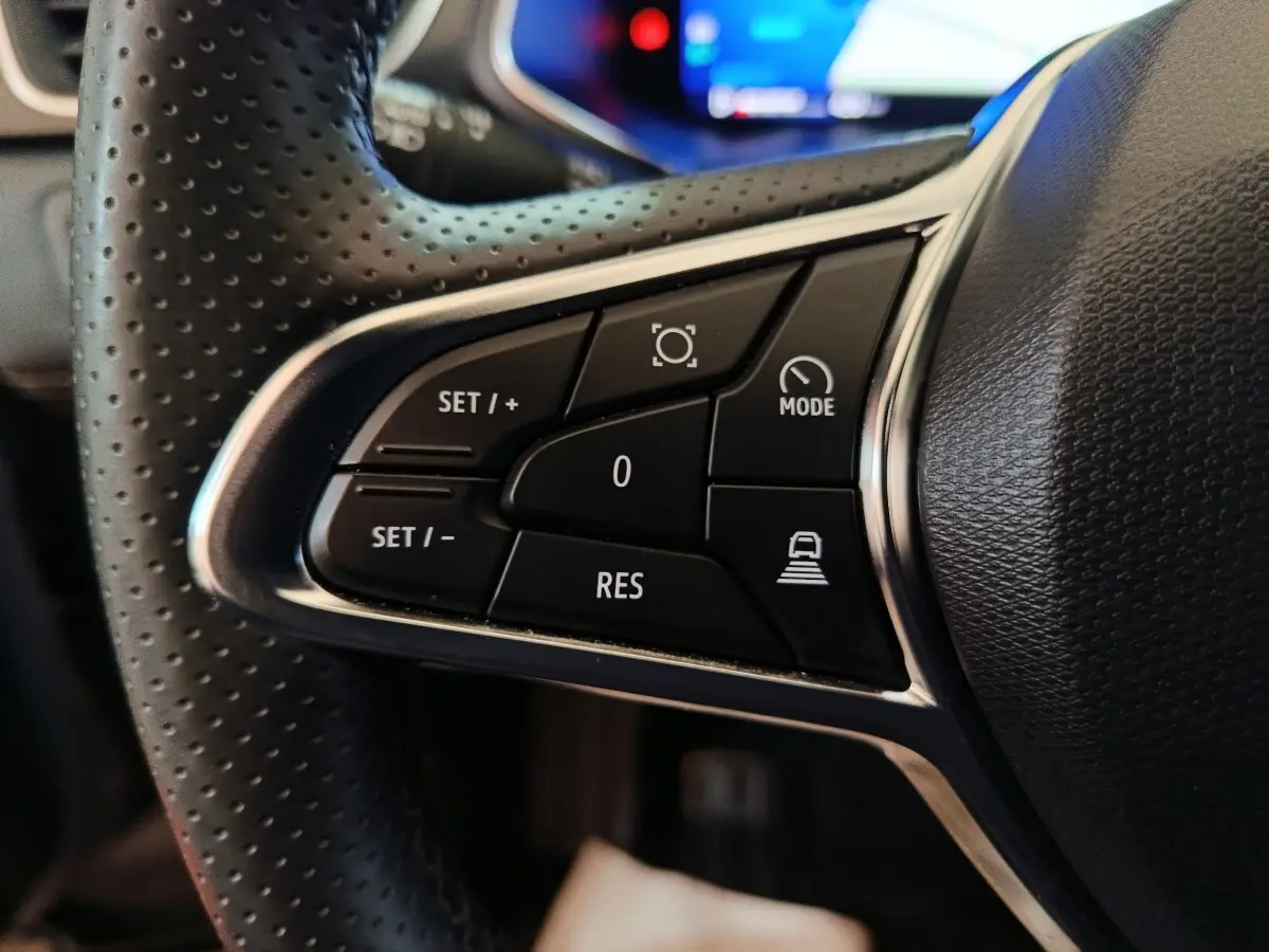 Gros plan sur les commandes noires du volant perforé côté gauche du Renault Symbioz hybride 2025, avec chrome brillant.