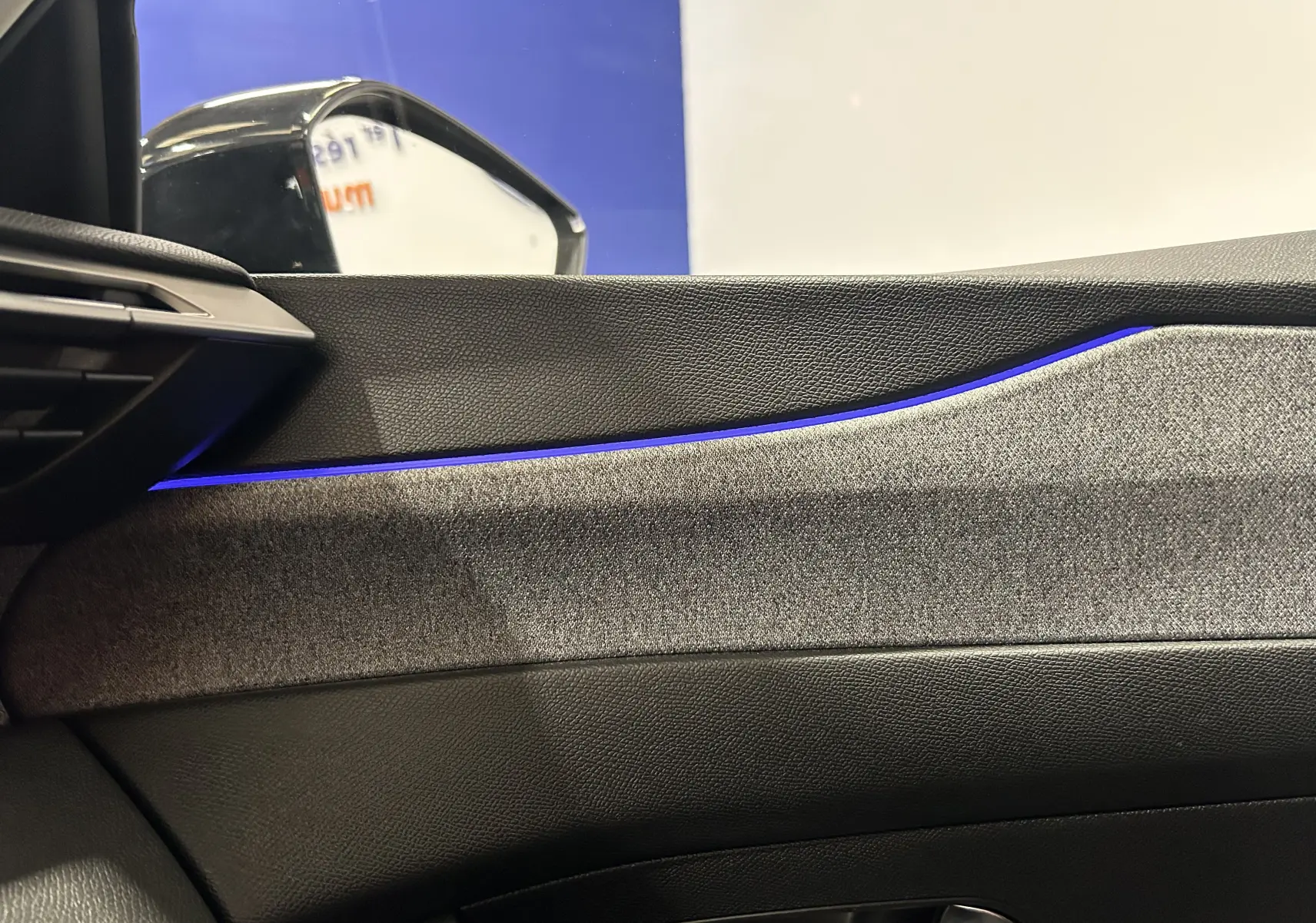 Détail intérieur côté conducteur de la Peugeot 308 gris, avec éclairage d'ambiance bleu sur la garniture de porte.