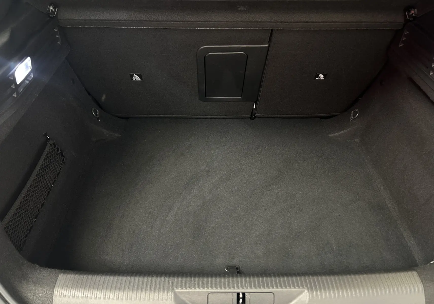 Vue intérieure du coffre spacieux et propre de la Peugeot 308 gris, avec éclairage et filet de rangement latéral.