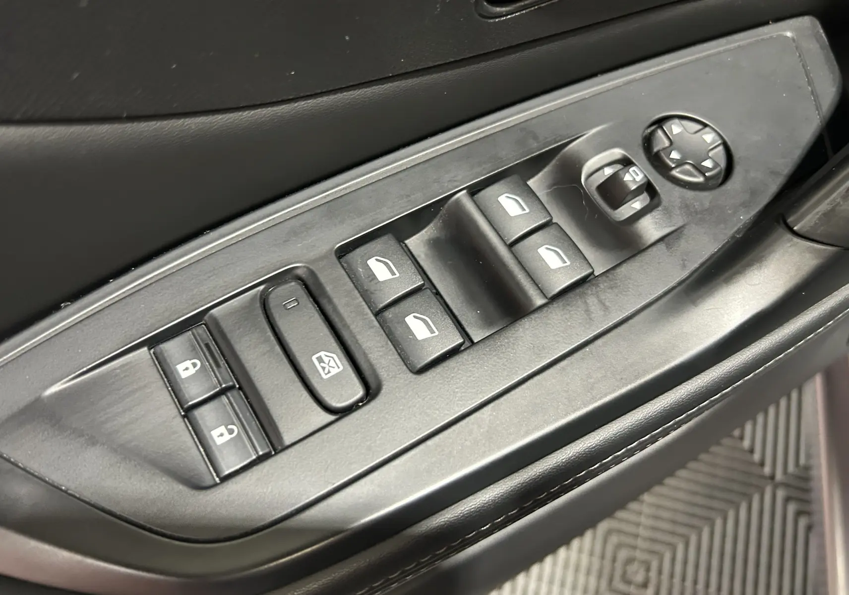 Gros plan sur les commandes de lève-vitres et rétroviseurs côté conducteur d’une Peugeot 308 gris, intérieur noir.
