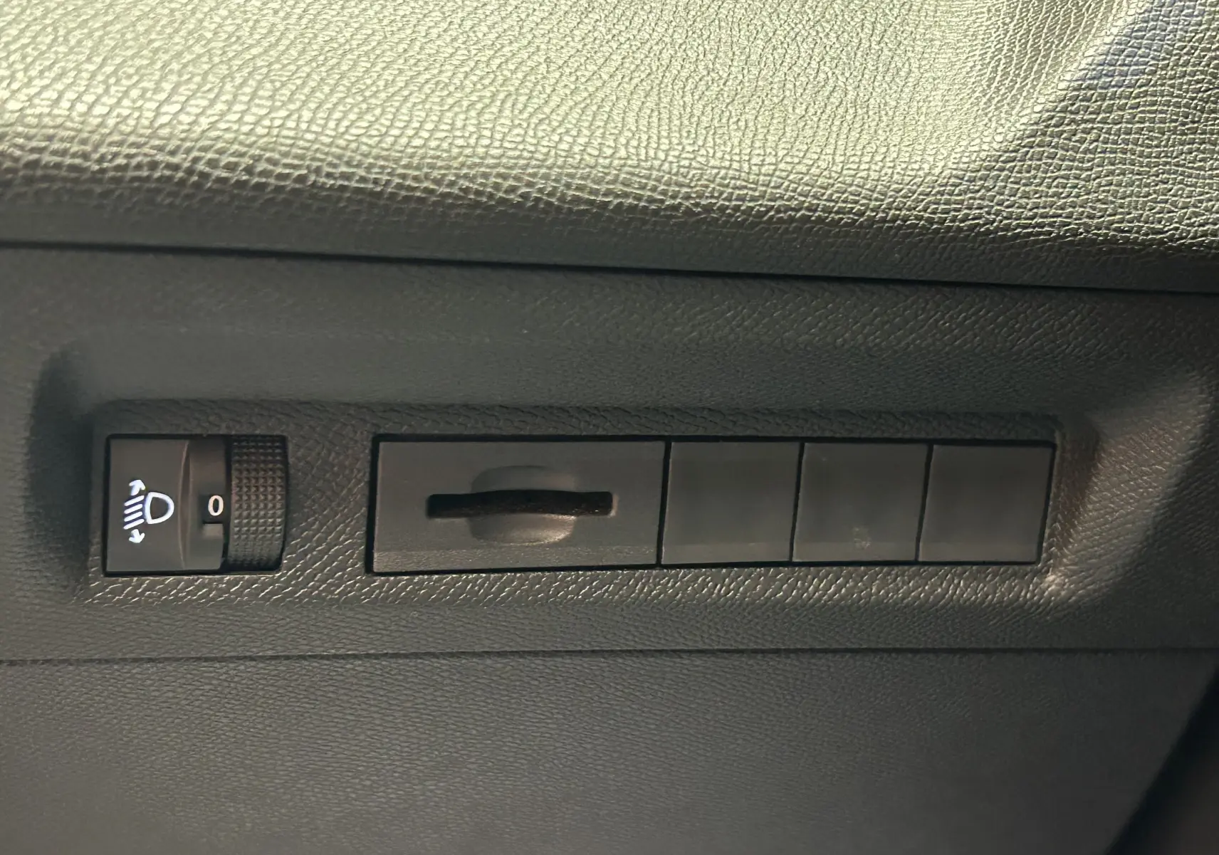 Détail intérieur montrant la molette de réglage des phares et plusieurs boutons noirs sur la planche de bord côté conducteur d’une Peugeot 308 gris.