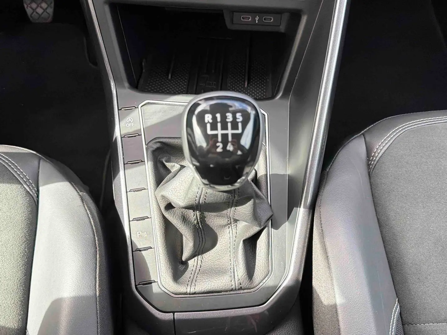 Vue rapprochée de la commande de boîte manuelle noire entourée de sièges en cuir gris dans une Volkswagen Polo 2025.