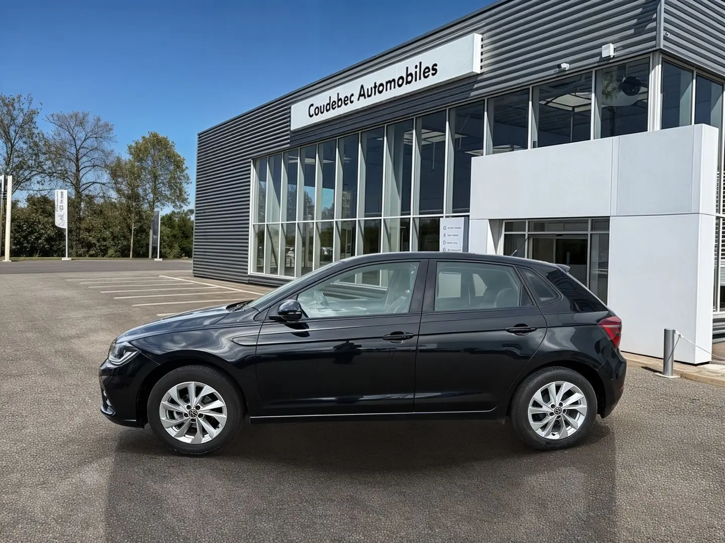 Vue de profil côté gauche d'une Volkswagen Polo noire 2025 garée devant un bâtiment de concession.
