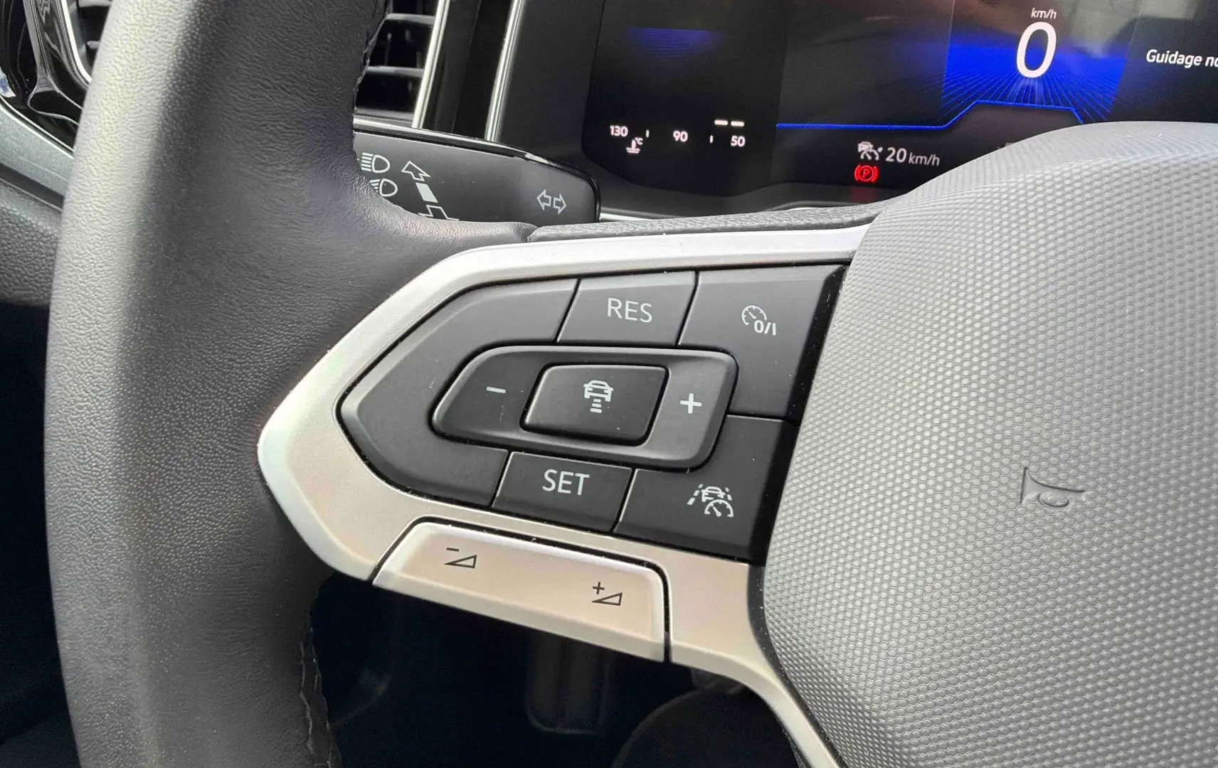 Gros plan sur le volant cuir gris de la Volkswagen Polo 2025, avec commandes du régulateur adaptatif et tableau de bord digital.