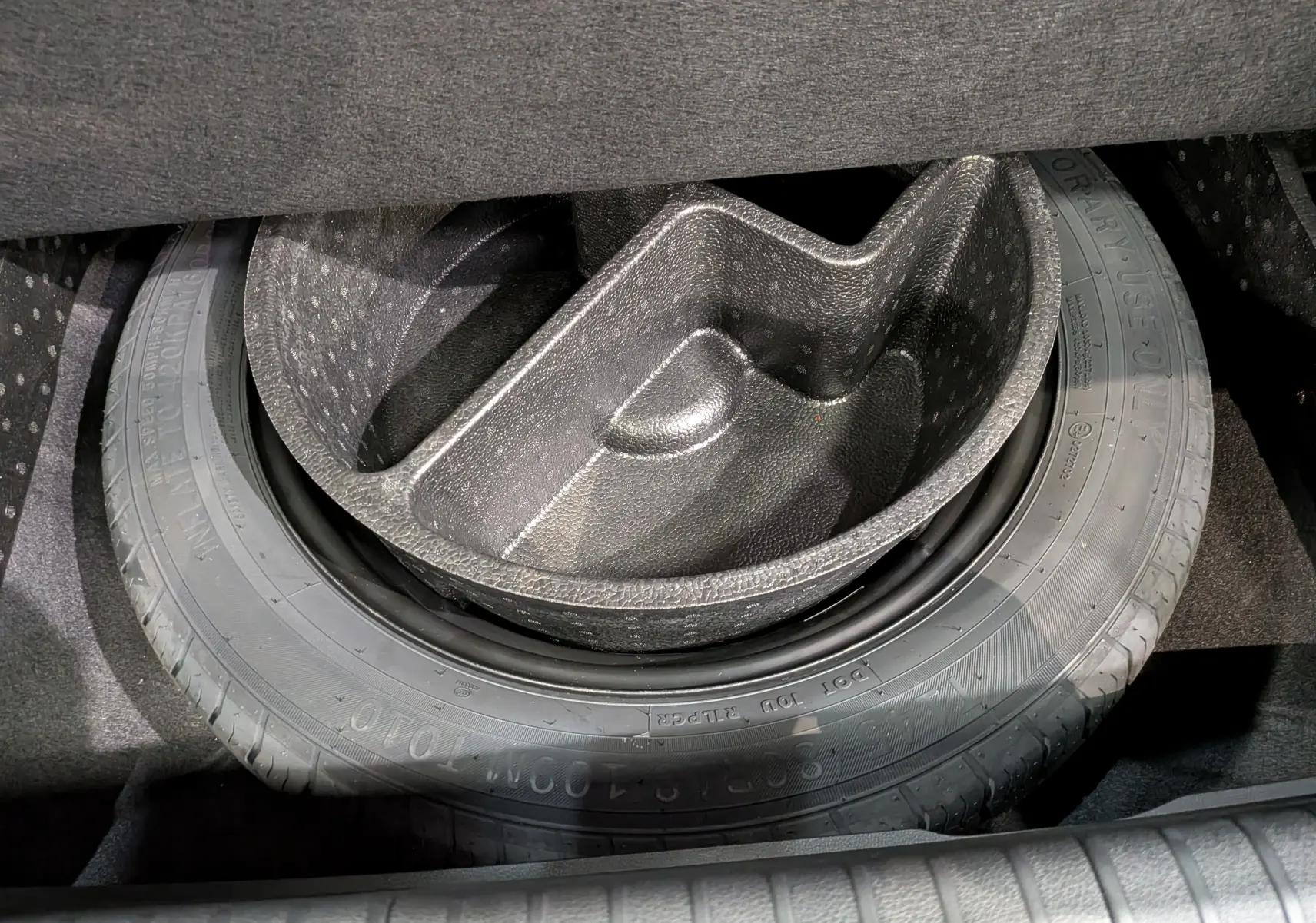 Gros plan sur la roue de secours et son rangement en mousse dans le coffre d'une Renault Rafale gris schiste satin.