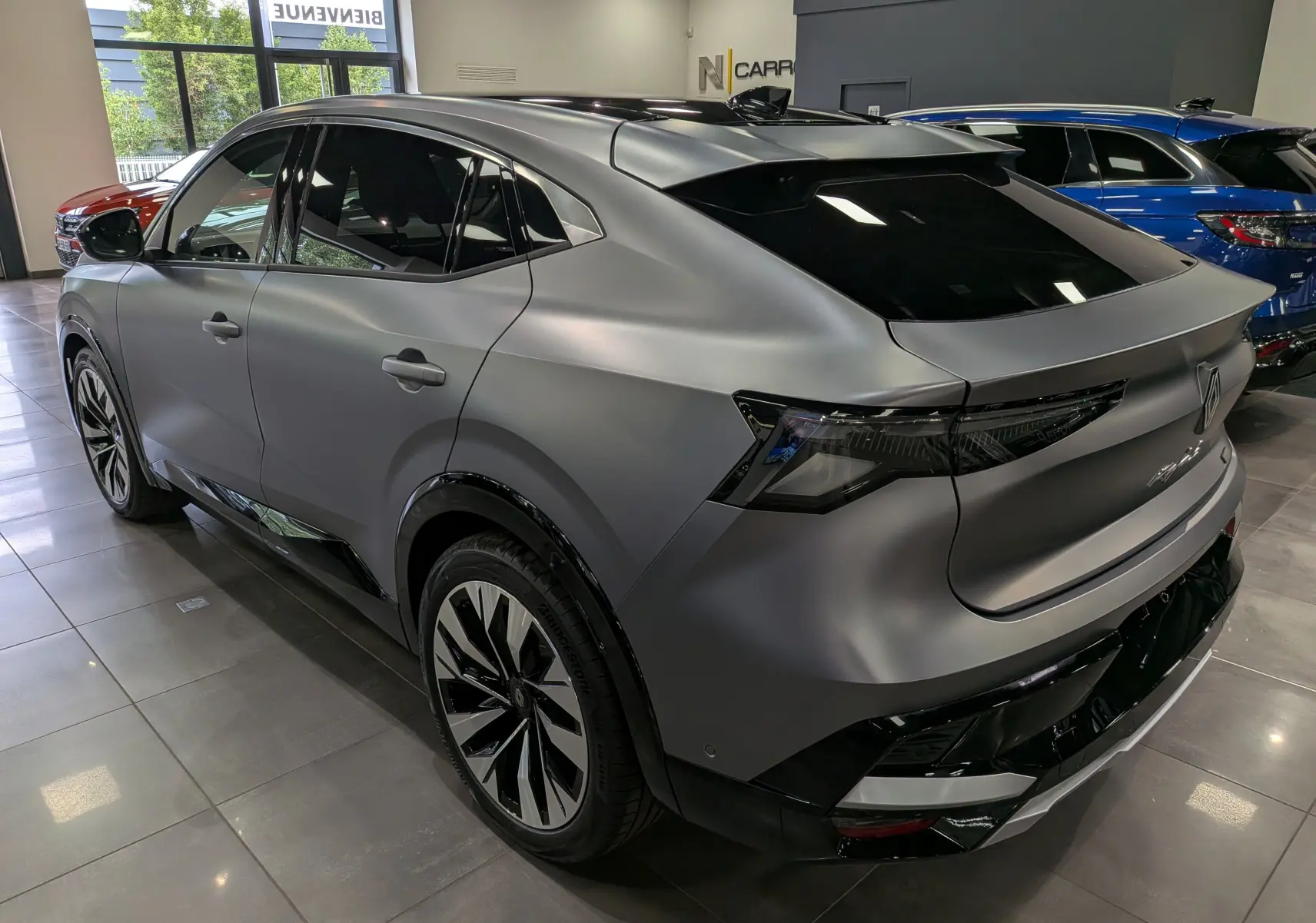 Vue 3/4 arrière droite du Renault Rafale E-Tech gris schiste satin avec jantes bicolores et vitres teintées en showroom.