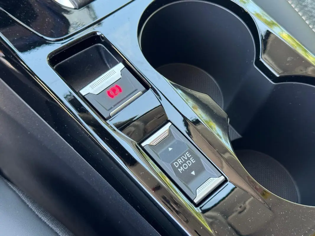 Gros plan sur la console centrale noire de la Peugeot 208 Hybrid 110 e-DCS6 Allure avec bouton frein à main électrique et mode de conduite.