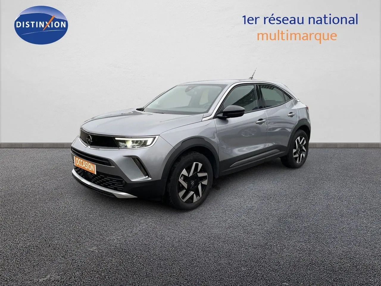 Opel Mokka gris Artens métal en 3/4 avant droit avec jantes noires et phares LED allumés sur fond neutre.