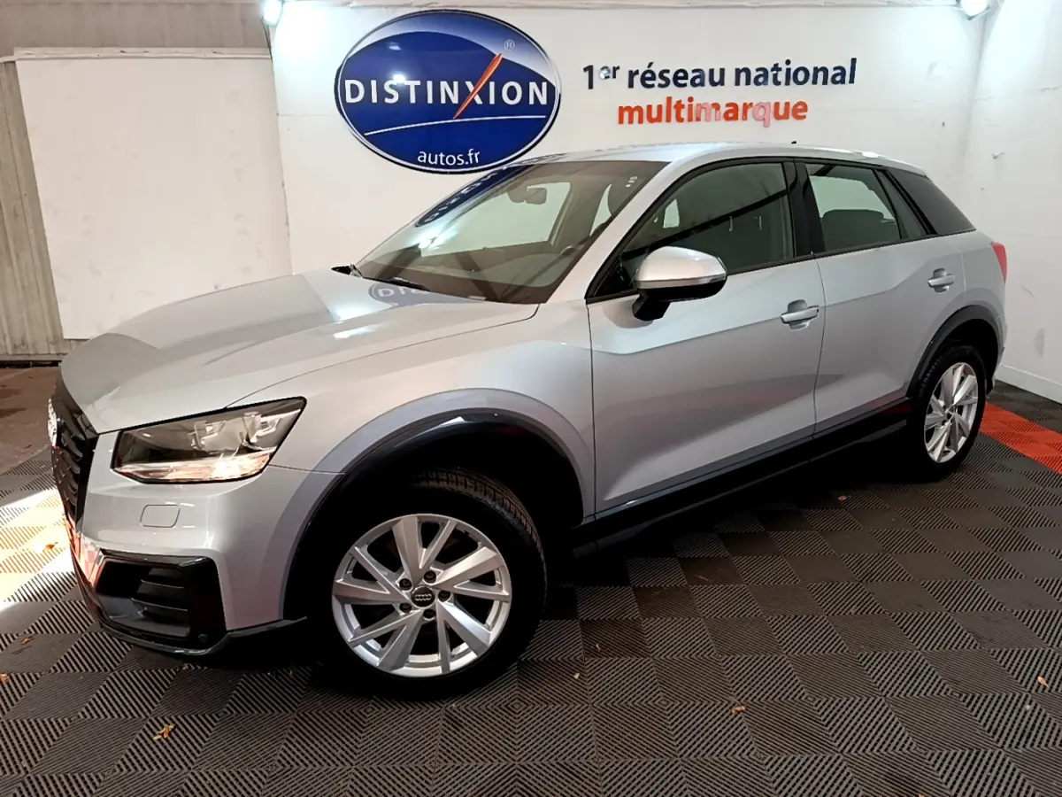 Audi Q2 35 TDI gris clair vue 3/4 avant droit en intérieur avec jantes alliage et phares allumés.