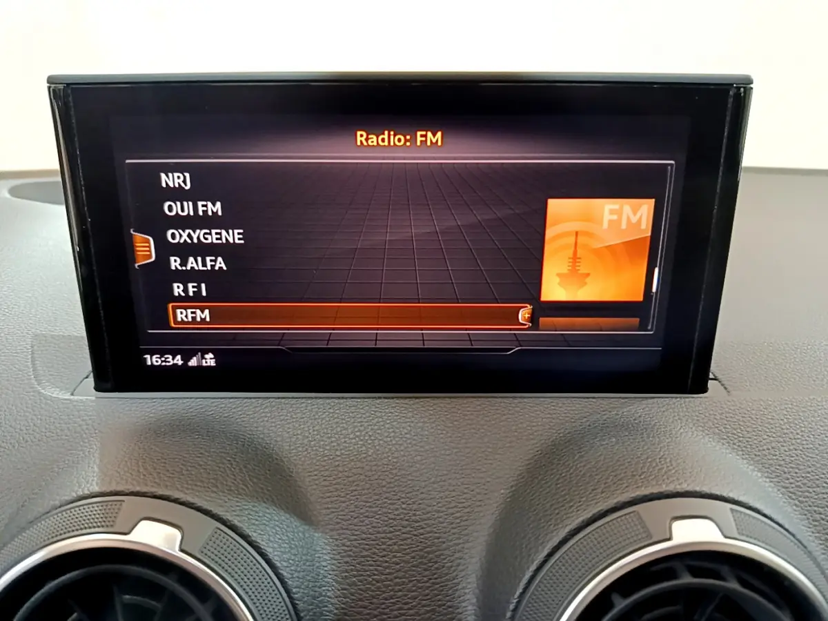 Écran central de l'Audi Q2 35 TDI 150 Design 2020 affichant les stations FM, avec aérateurs ronds en dessous.