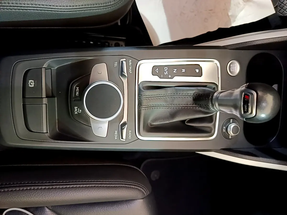 Vue rapprochée de la console centrale noire de l'Audi Q2 35 TDI 150 Design avec levier de vitesses automatique et molette de contrôle multimédia.