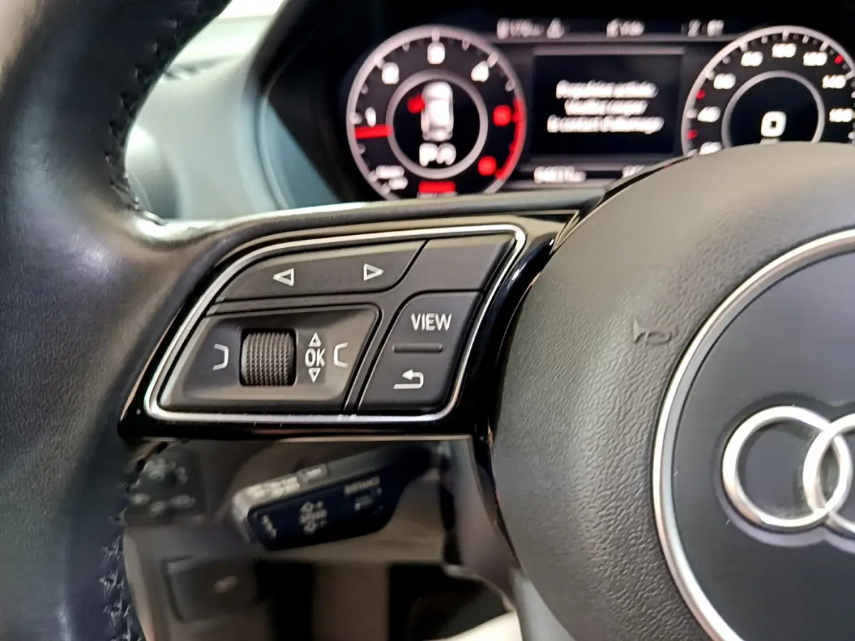 Gros plan sur le volant cuir noir de l'Audi Q2 35 TDI 150 Design avec commandes multifonctions et tableau de bord numérique.