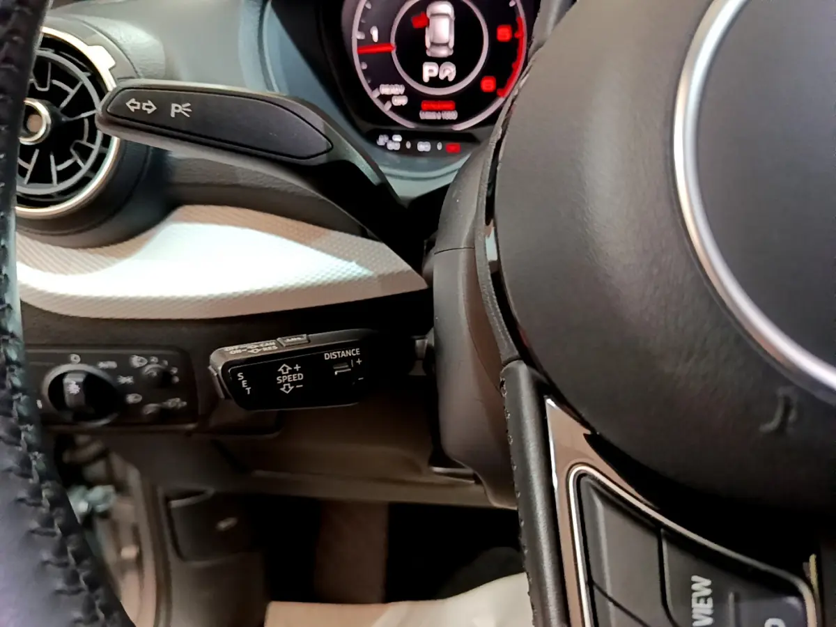 Gros plan sur le volant cuir et commandes au volant côté gauche de l’Audi Q2 35 TDI 150 Design gris clair, avec tableau de bord numérique.