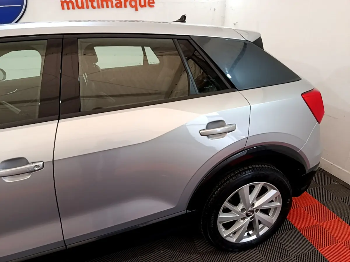 Vue latérale droite sur l'arrière d'un Audi Q2 gris clair, avec jante alliage et vitre arrière teintée.