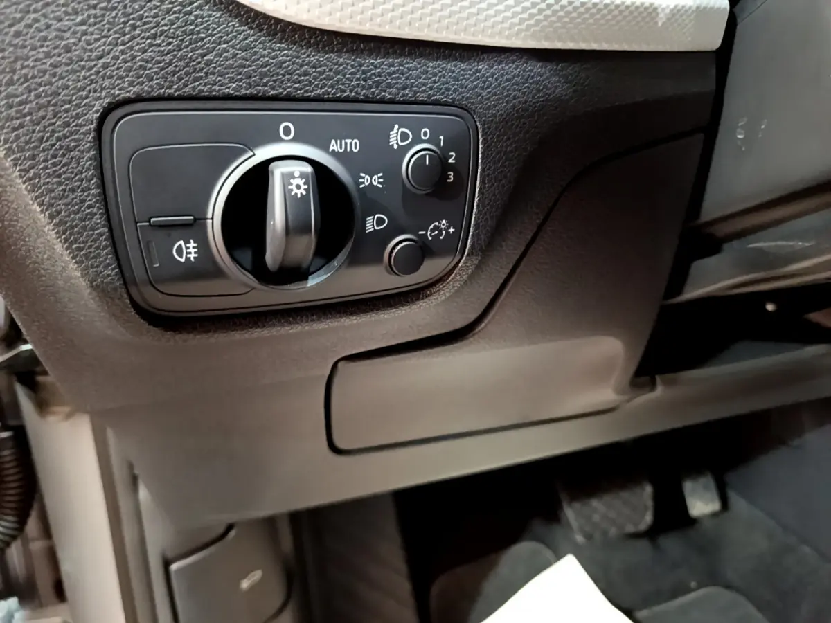 Gros plan sur le panneau de commande des phares à gauche du volant dans l'Audi Q2 35 TDI 150 Design gris clair de 2020.