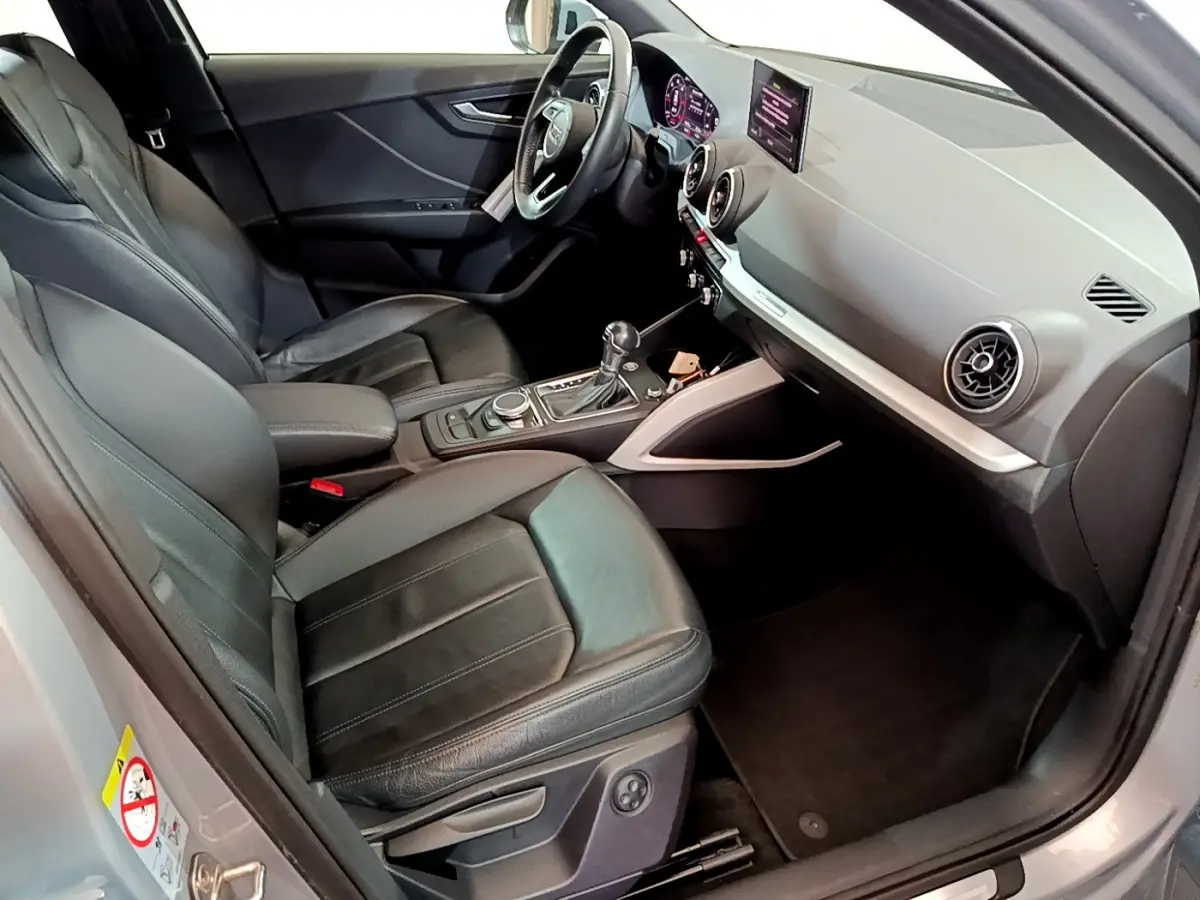 Vue intérieure côté conducteur de l'Audi Q2 gris clair 2020, sièges cuir noirs et tableau de bord moderne avec écran central.