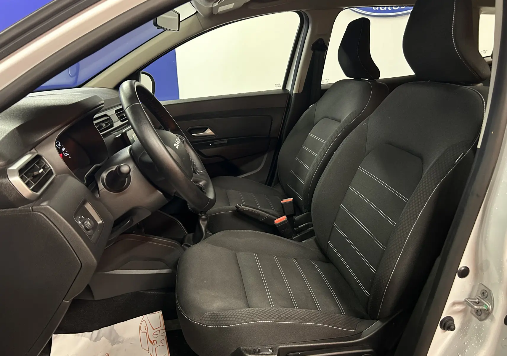 Vue intérieure côté conducteur du Dacia Duster blanc 2024, mettant en valeur les sièges chauffants en tissu noir avec coutures contrastées.