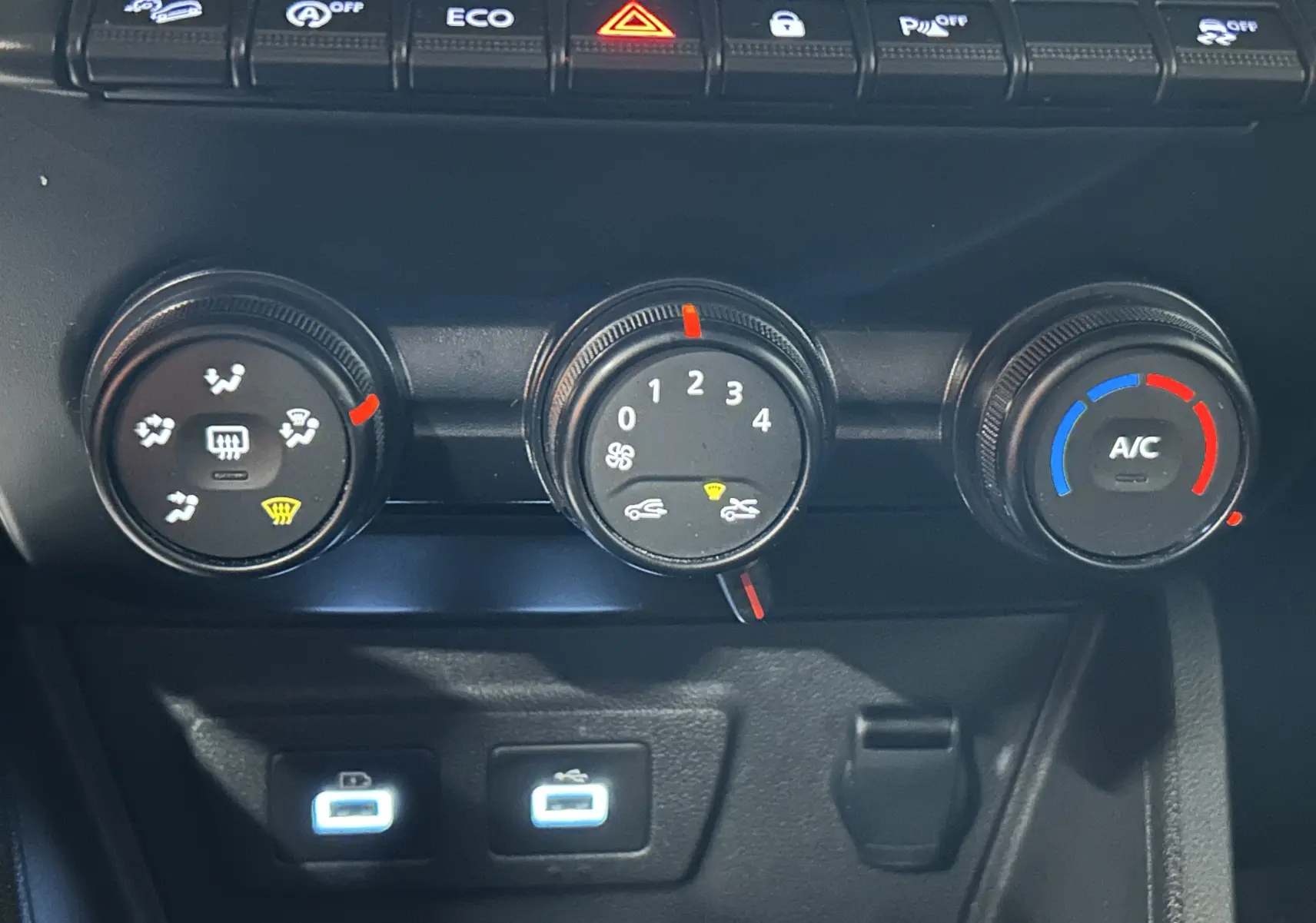 Vue rapprochée du tableau de bord du Dacia Duster 2024 montrant les commandes de climatisation et deux ports USB éclairés.