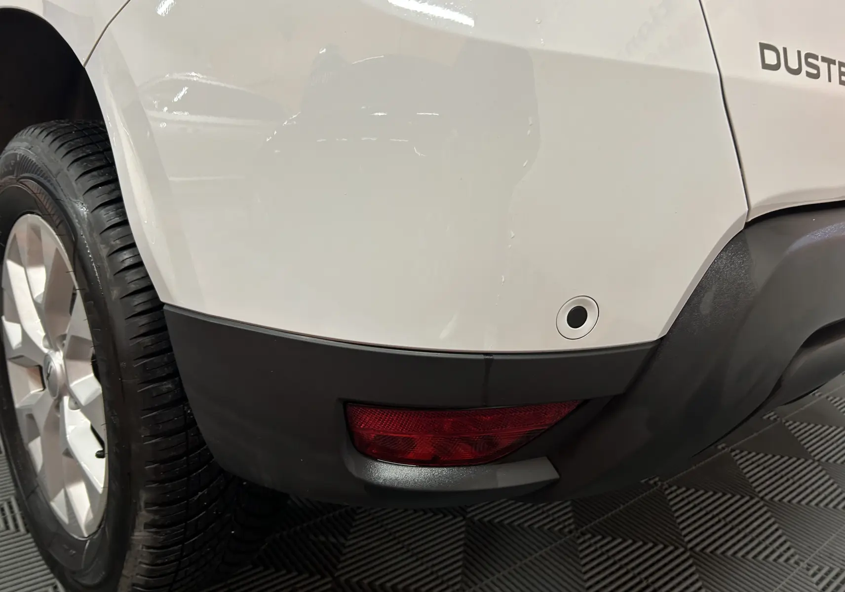 Gros plan sur l’angle arrière droit blanc du Dacia Duster 2024, avec feu arrière et capteur de recul visibles.