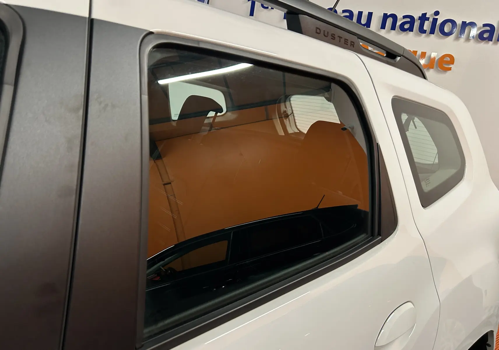 Vue latérale droite sur la porte arrière blanche d'un Dacia Duster 2024 avec toit et montant noir, badge Duster visible.