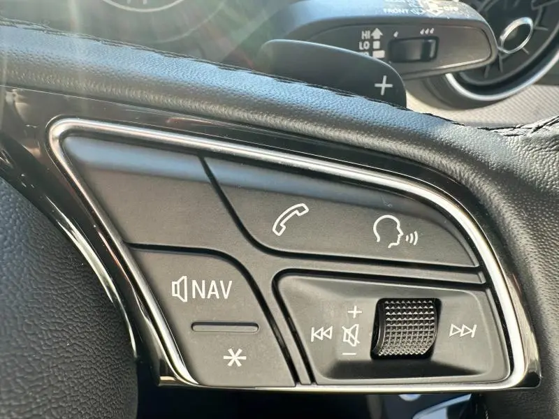 Gros plan sur les commandes multifonctions du volant cuir noir de l'Audi Q2 blanc, avec boutons navigation et appel.