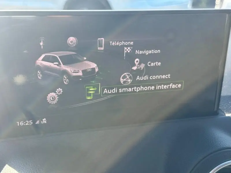 Écran multimédia intérieur affichant l'interface Audi smartphone avec une vue stylisée du Q2 blanc en 3/4 avant.