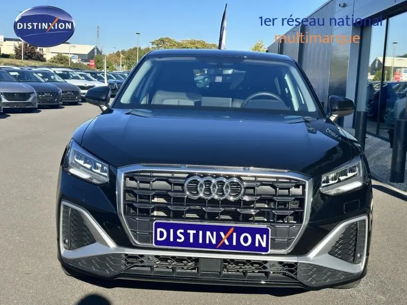 Vue avant d'un Audi Q2 noir avec calandre large et phares LED, stationné en extérieur devant un showroom.