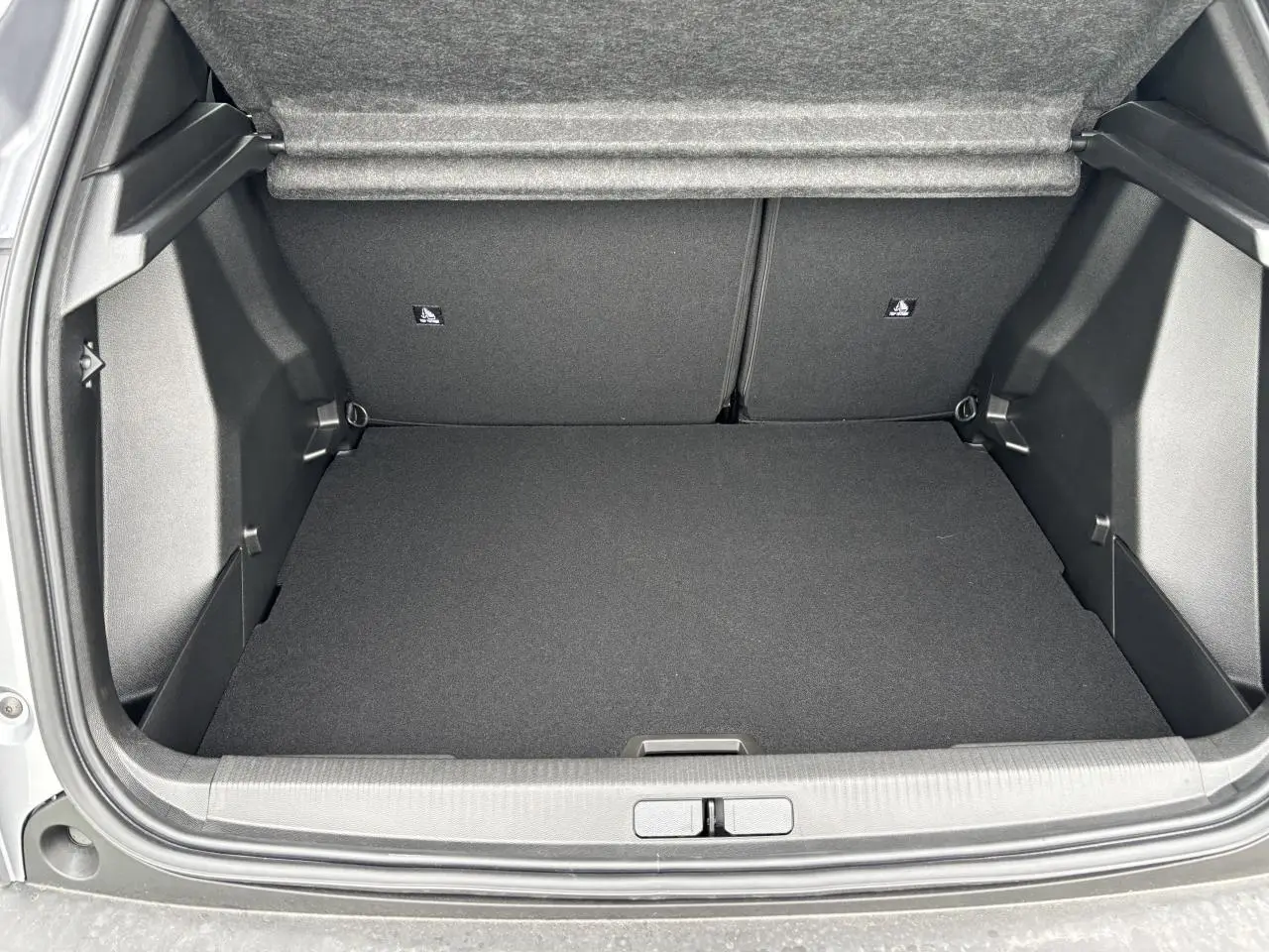 Coffre ouvert vu de l'arrière d'une Peugeot 2008 gris Artense avec intérieur noir et banquette rabattable.
