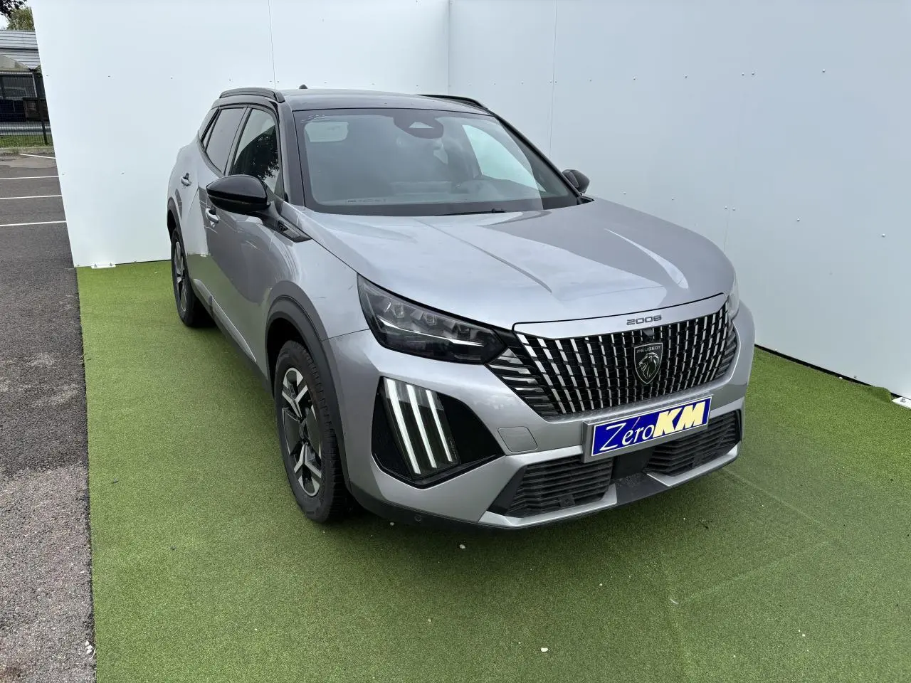 Peugeot 2008 gris Artense toit noir en 3/4 avant droit, calandre verticale et feux LED griffes visibles.