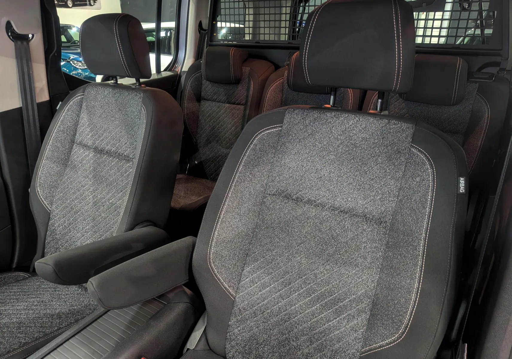 Gros plan sur les sièges avant et arrière en tissu gris du Peugeot Rifter 2025, version Allure, avec appuie-bras côté droit.