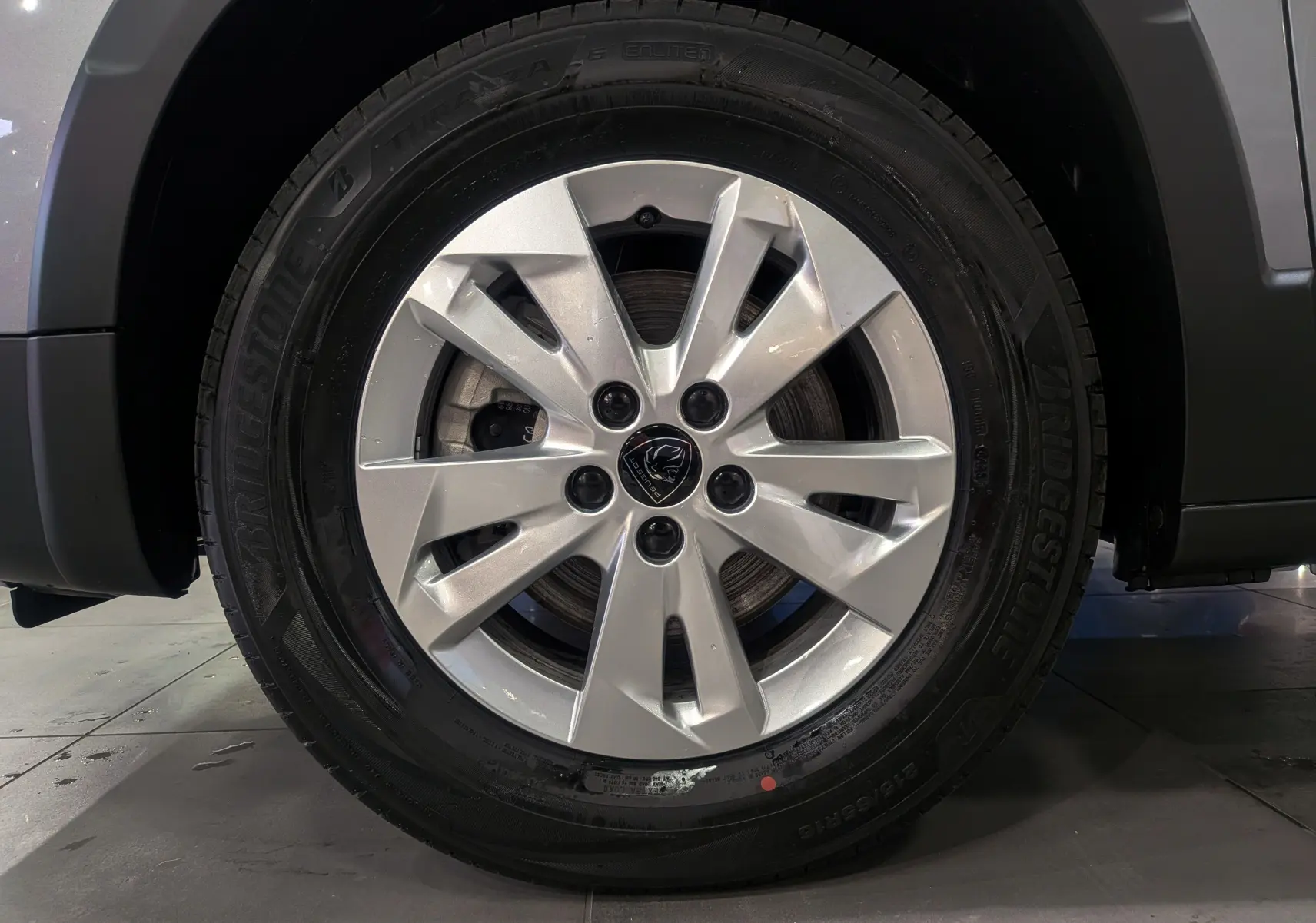 Gros plan sur la roue avant droite avec jante alliage argentée du Peugeot Rifter gris acier 2025.