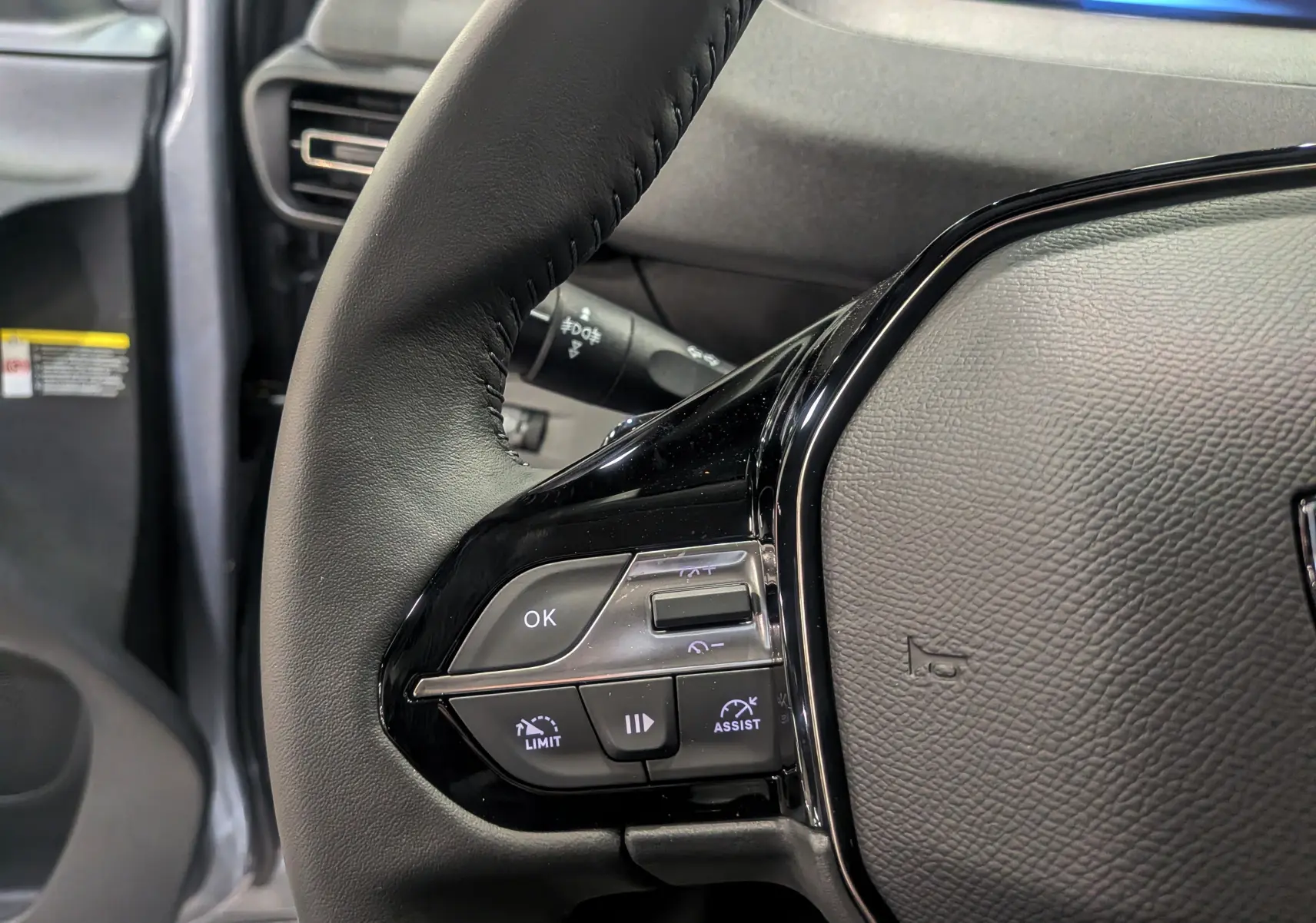 Gros plan sur le volant noir du Peugeot Rifter gris acier 2025, montrant les commandes multifonctions côté gauche.