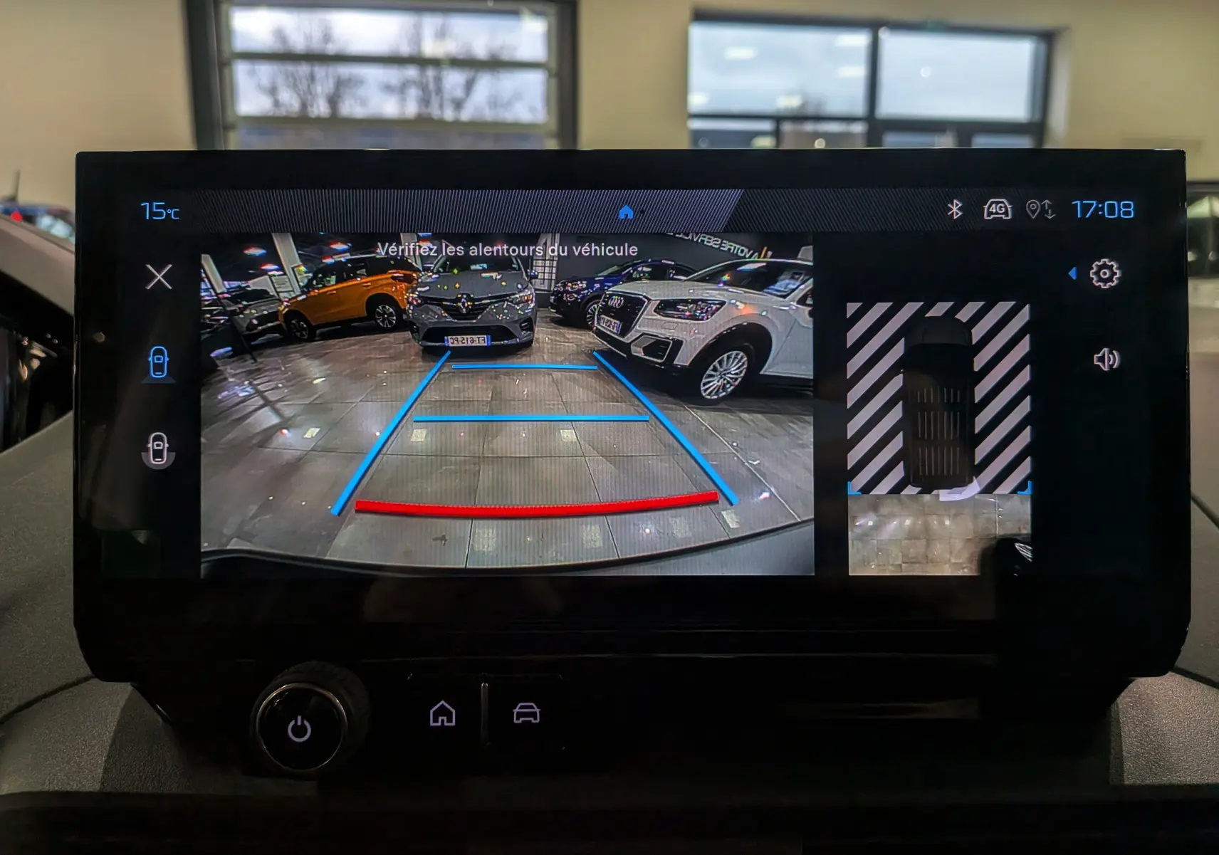 Vue de l'écran de recul du Peugeot Rifter gris acier 2025, affichant les lignes de guidage et la caméra 360° en intérieur showroom.