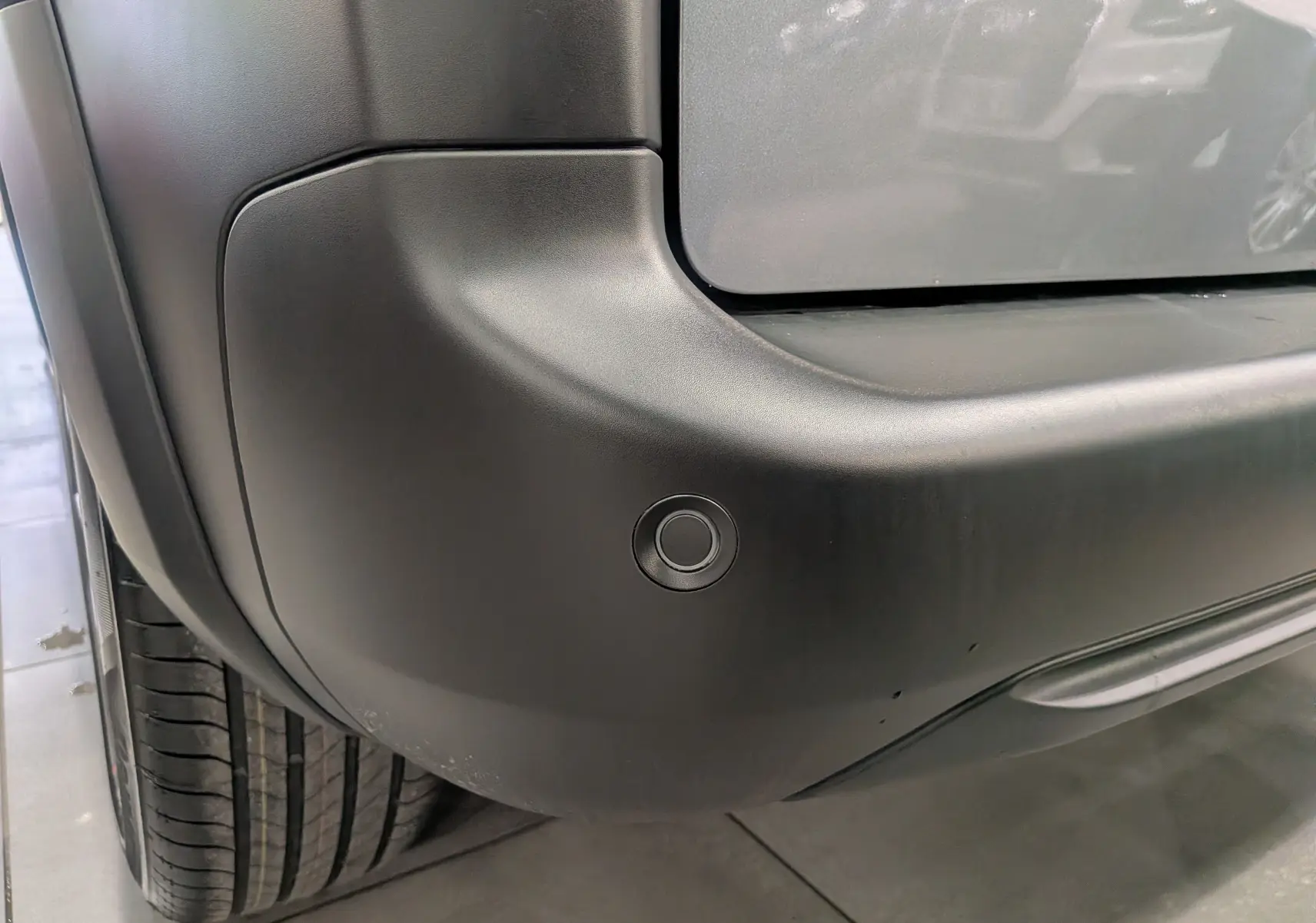 Gros plan sur le pare-chocs arrière gris acier du Peugeot Rifter 2025, mettant en valeur un capteur de stationnement circulaire.